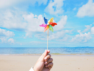 Close up hand holding colorful pinwheel over summer beach background.