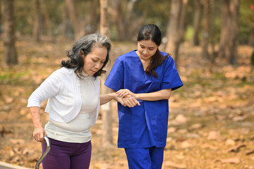 Image of caring female caregiver helping senior woman walking in the park. Assistance and rehabilitation concept