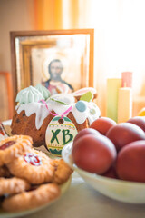 Easter cake with painted eggs, apples and cookies on table in home kitchen. Church icons and candle on background. Orthodox religion theme.