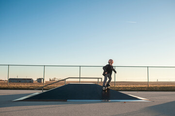 Young boy riding down pyramid ramp at the skate park on sunny day