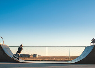 Young boy using half pipe ramp at the skate park on sunny day