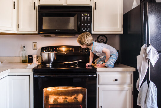 young boy sitting on counter looking at oven timer while cookies bake
