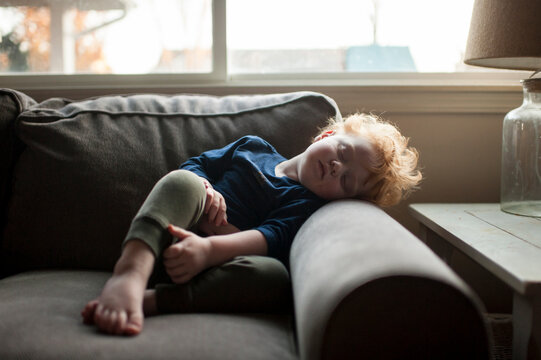 Young boy sleeping in funny position on couch at home