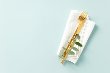 Gold Cutlery with eucalyptus branches on napkin over blue Background. Minimalistic design. Copy Space banner