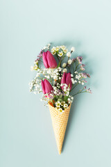 Ice cream cone with beautiful flowers on blue background flat lay