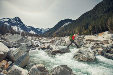 Backpacker jumps boulders to cross a raging river in the wilderness.