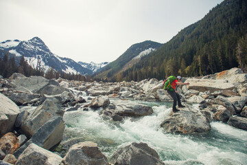 Backpacker jumps boulders to cross a raging river in the wilderness.