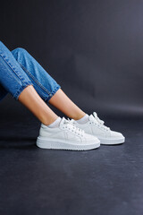 Close-up of female legs in jeans and casual white sneakers. Women's comfortable casual shoes. White leather women's sneakers