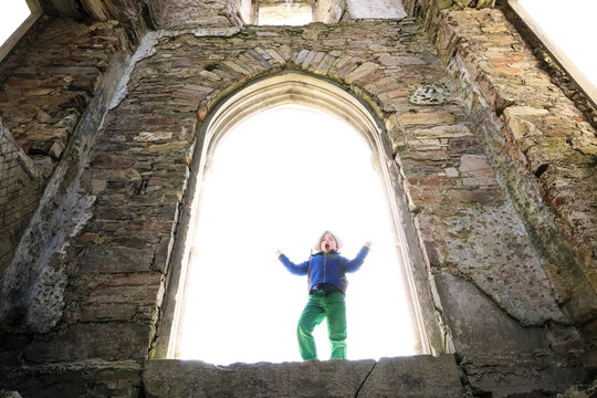 Young Boy Does Silly Pose While Standing in Large Stone Castle Window