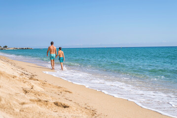 Rear view of father and son walking along the beach in a sunny day