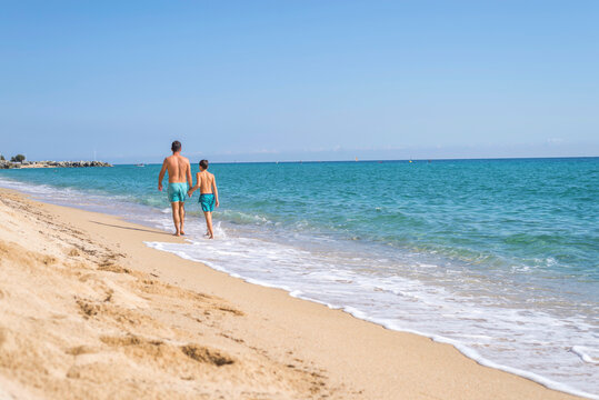 Rear view of father and son walking along the beach in a sunny day