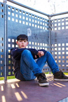 Portrait of young boy sitting looking camera,leaning on metallic fence