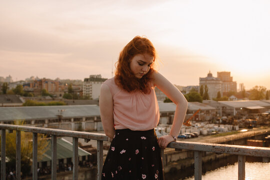 Teenage girl with red hair standing on bridge at sunset