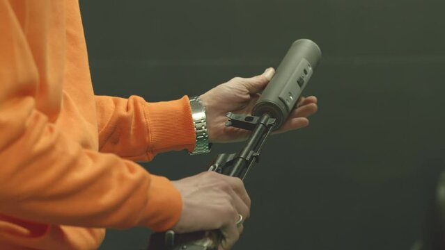A man screws a silencer on a Kalashnikov assault rifle