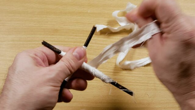 A man makes a voodoo doll from branches and a white ribbon, close-up.