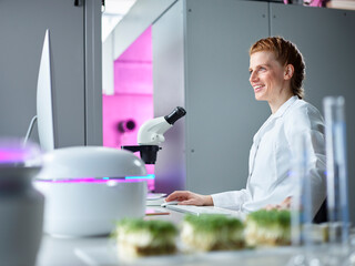 Smiling scientist in front of microscope on desktop at laboratory