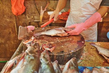 A fishmonger in Chow Kit Road Market in Kuala Lumpur, Malaysia closely while cleaning the fish. The market was a bustling center of commerce, full of shoppers.