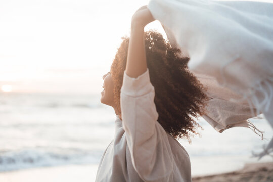 Happy young woman holding scarf at beach