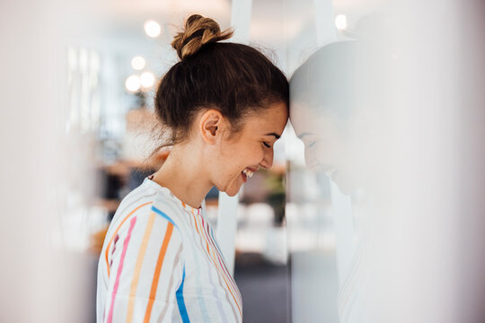 Happy businesswoman leaning forehead on wall in office