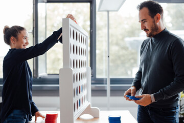 Happy businesswoman with colleague playing connect four dots game in office