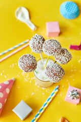 Festival birthday background with delicious homemade popcake coconut chocolate cake pops on a yellow background, festival desserts, tasty food