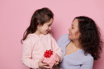 Mother and daughter have fun together, smiling, embracing, posing with a cute gift on isolated pink background. International Women's Mother's Children's Day concept. Family People Human relationships