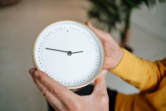 Hands of senior man holding clock at home