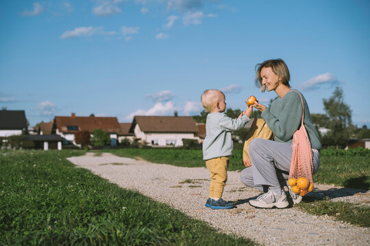 Smiling woman giving apple to son on footpath