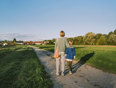 Woman with arm around son walking on footpath