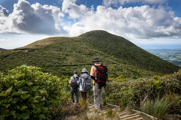 Three people hiking Pouakai circuit with views of the Taranaki coastline, Egmont National Park. New Zealand.