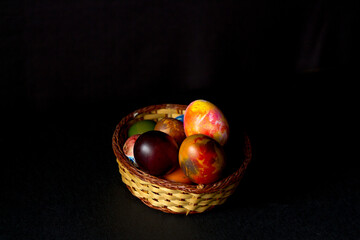 Colored easter eggs in a wooden basket on a black background