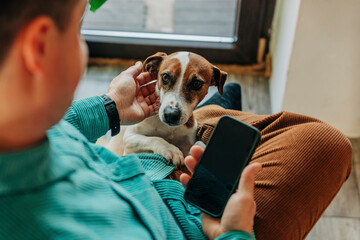 Man holding smart phone and stroking dog at home