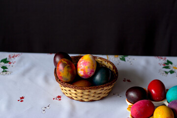 Colored easter eggs in a wooden basket at a white tablecloth on a black background
