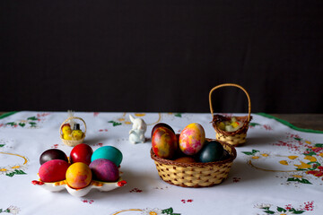 Colored easter eggs in a wooden basket at a white tablecloth on a black background