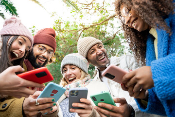 Obraz premium Group of happy multi ethnic friends sharing social media content on smart phone, winter outdoors