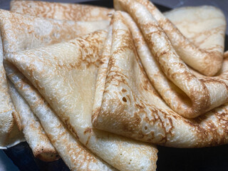 Fresh and delicious pancakes, neatly folded in envelopes, lay on a black plate. Pancakes close-up