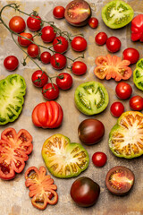 Different types of tomato, tomato halves and a sprig of cherry tomatoes.