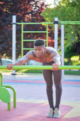 Young fit shirtless black man doing push-ups on a bar in a calisthenics park outdoors on sunny day. Fitness and sport lifestyle.