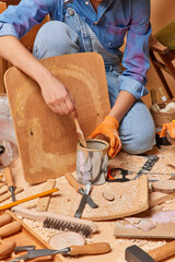 Cropped shot of unrecognizable craftswoman paints wooden surface for chair surrounded by variety of...