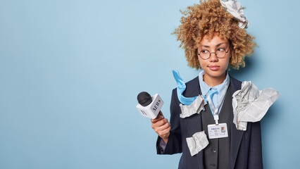 Horizontal shot of serious thoughtful woman correspondent dressed in formal suit holds microphone...