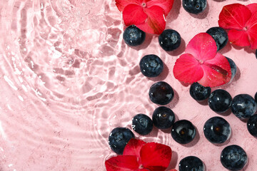 Blueberry and flowers in water on pink background