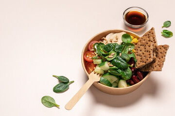 Chicken fillet, tomatoes, cucumbers, beans, corn, spinach in cardboard bowl on light beige background. Healthy food delivery, takeaway food, diet concept