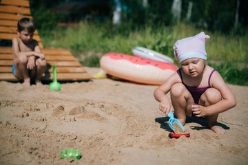 children playing with sand on summer day on beach and have a small fight - obrazy, fototapety, plakaty