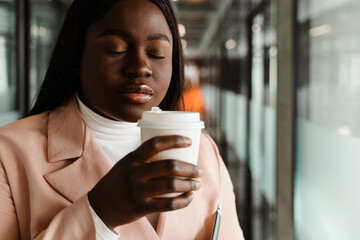 Young african american woman in suit drinking coffee in office corridor