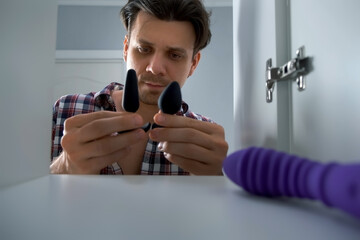 Young man is choosing sex toys opening wardrobe door at home. Using toys to get pleasure in sex. Active and diverse sex life.