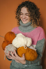 Smiling curly haired woman wearing warm sweater holding many colorful yarn clews in her hands...
