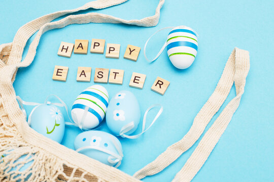 inscription happy easter with colorful painted eggs and cotton string bag on blue background
