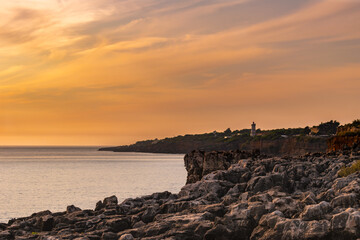 Limestone rock formation in contrast at sunset with Guia cliff and lighthouse on the horizon at Boca do Inferno, Cascais PORTUGAL