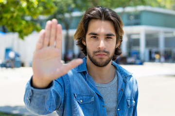 Serious mexican young adult man with beard gesturing stop with hand