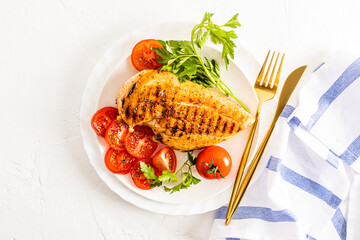 top view of a white serving plate with grilled chicken breast fillet with cherry tomato slices and parsley. white background. a copy space.